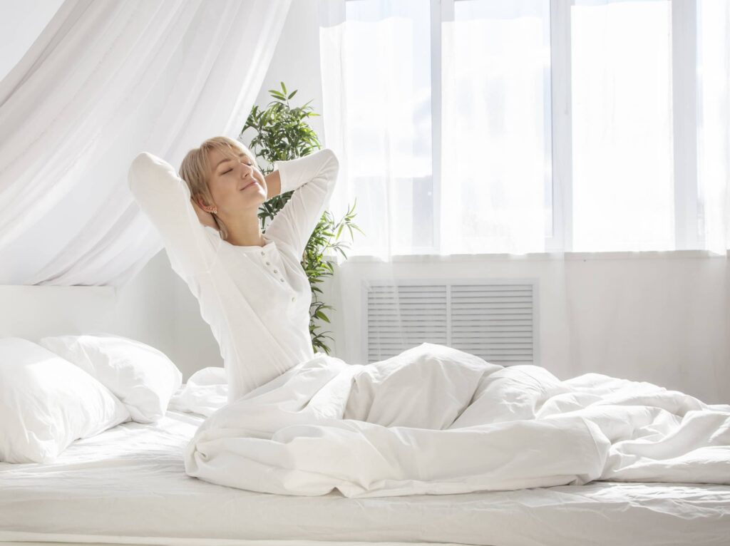 beautiful woman has woken up and is sitting on a white bed, Better Sleep Council